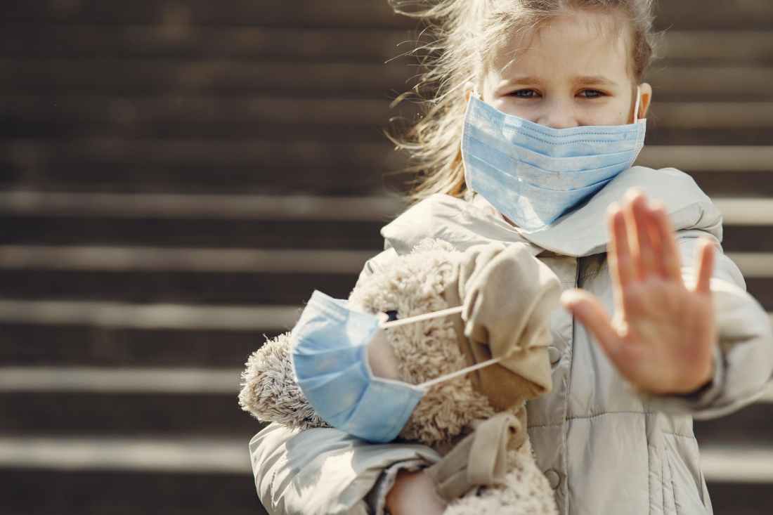 serious girl in protective mask holding plush toy in mask and showing palm against steps